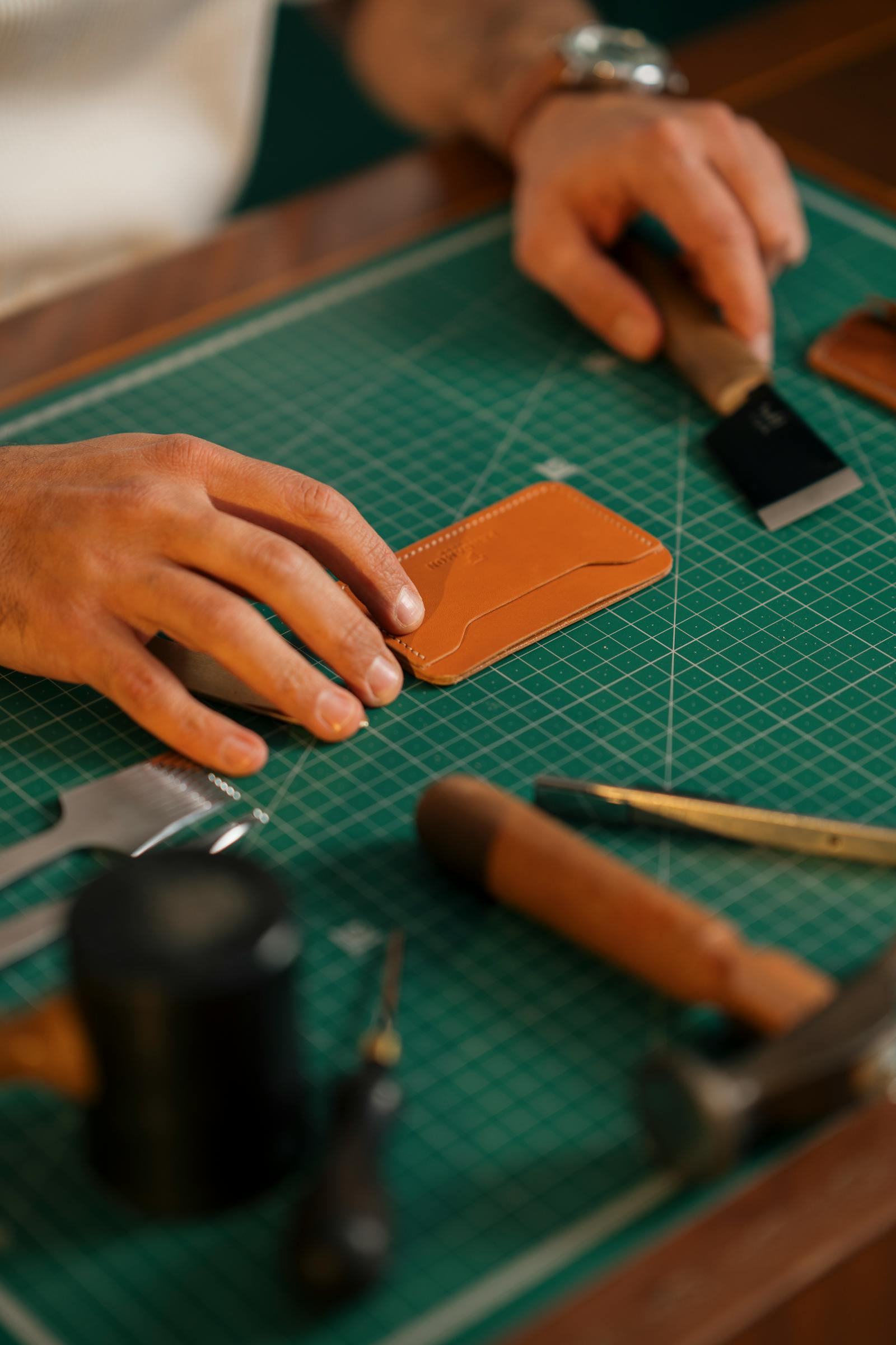Mani che lavorano un portafoglio in pelle su tappetino da taglio